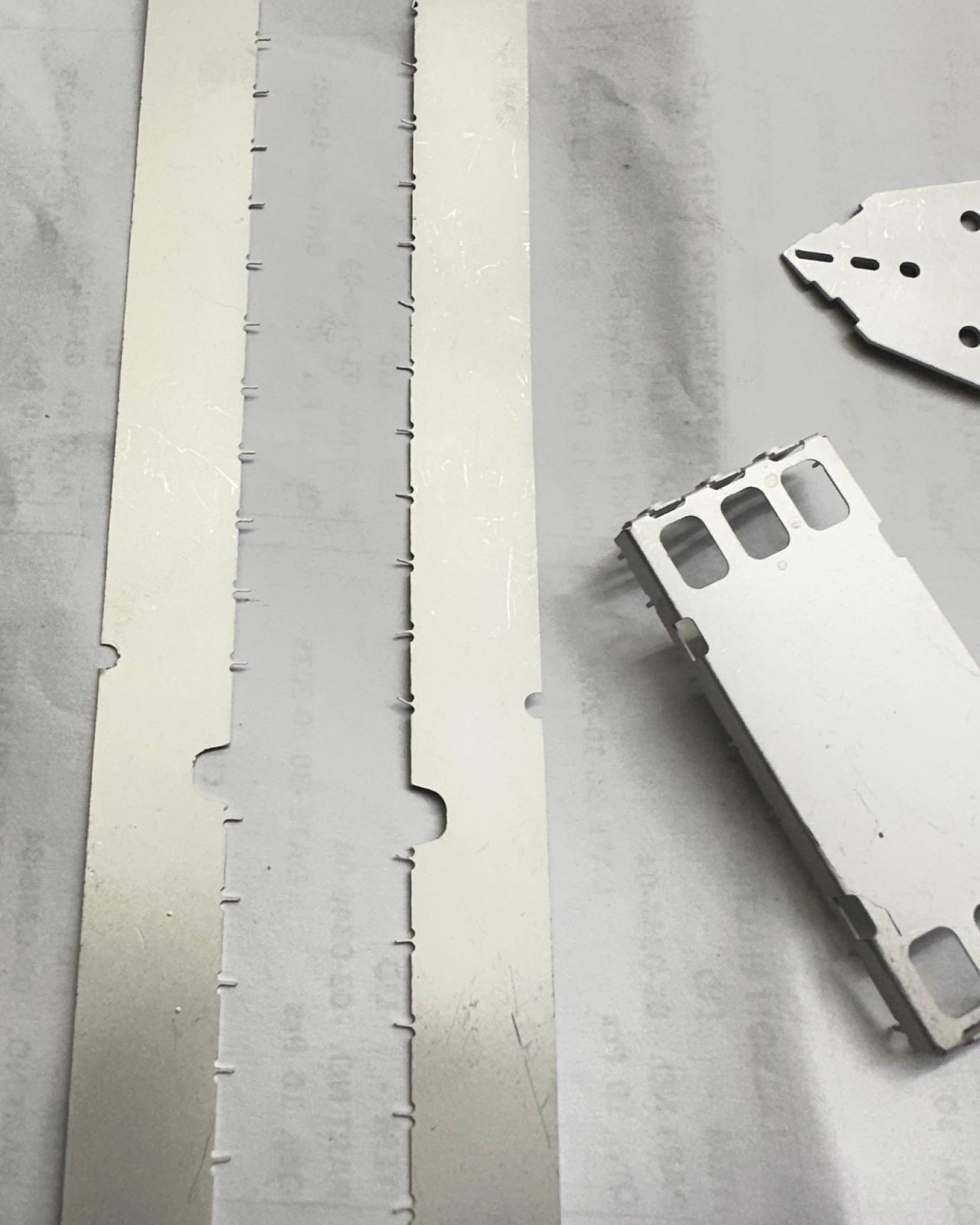 Two matte tin-plated stamped strips and a pressed frame on white paper